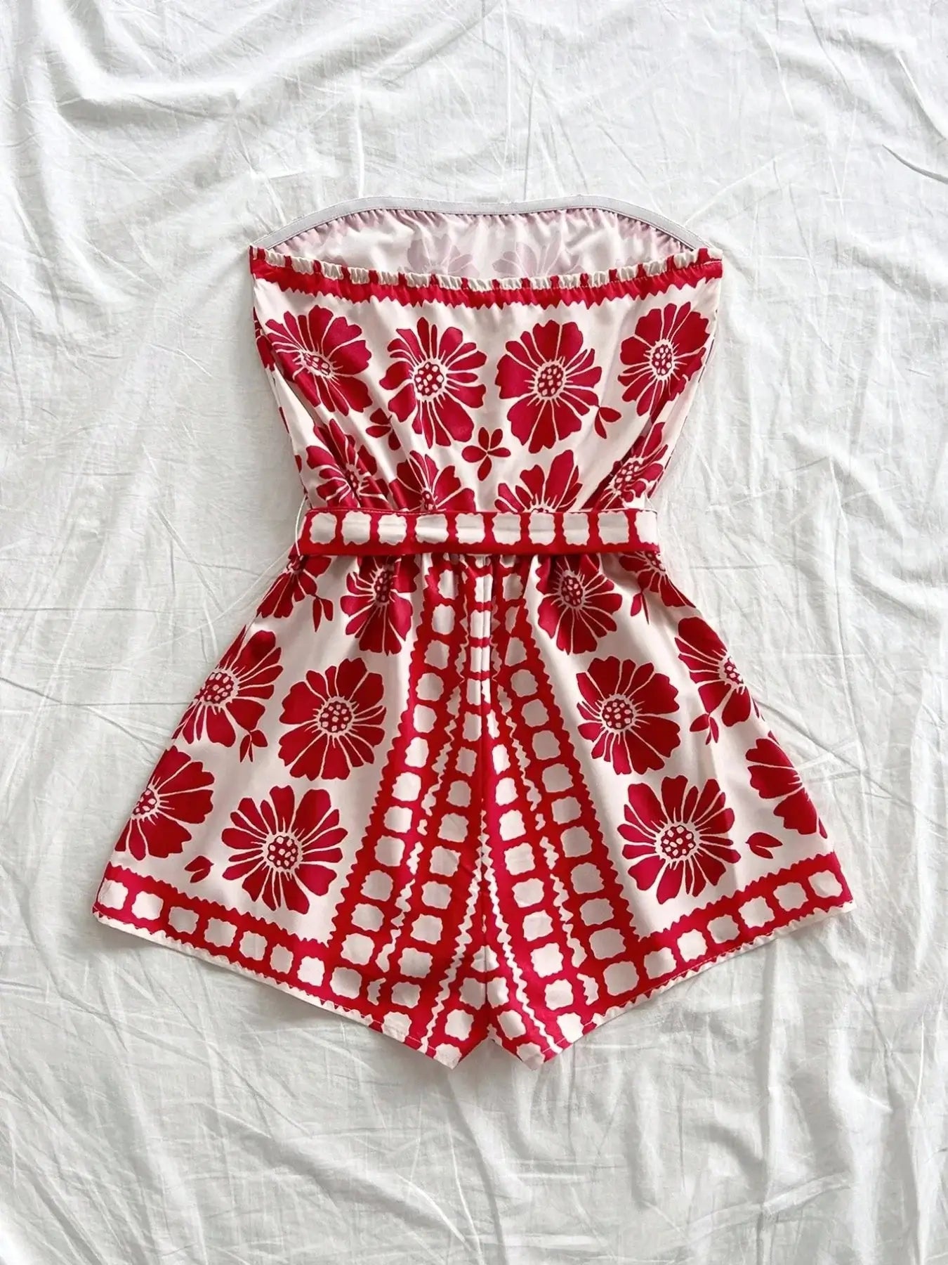 Printed tube tie waist romper with red floral design on a white background, featuring a belted style.