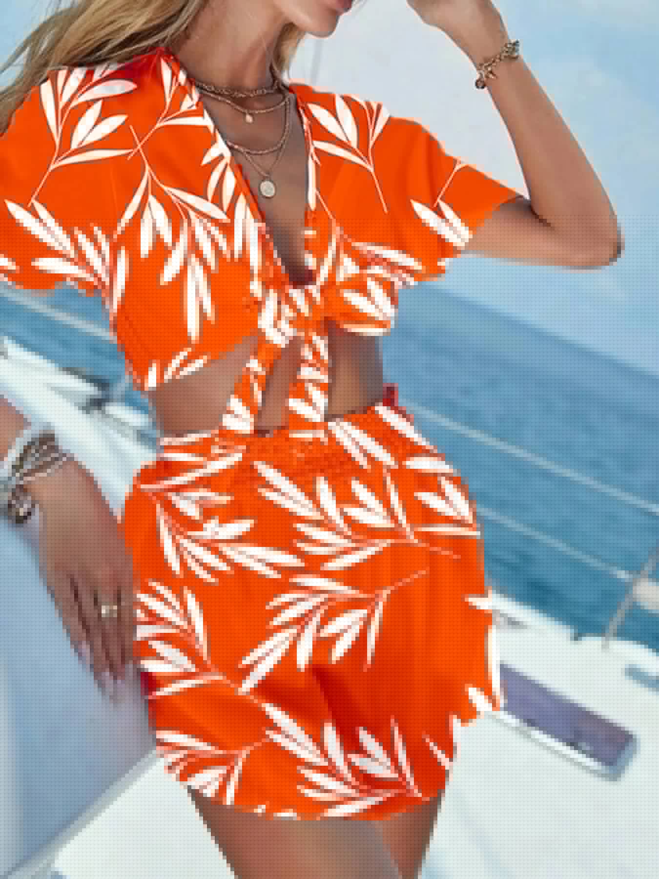 Model wearing a vibrant orange printed tie front top and shorts set on a boat with a scenic ocean view.