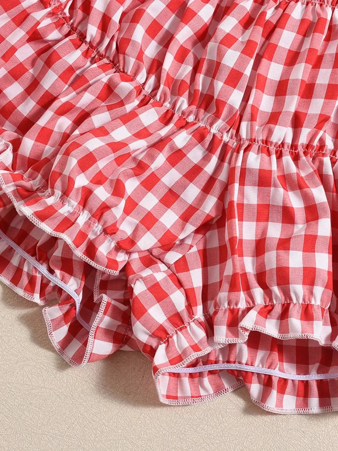 Close-up of a red and white plaid ruffled hem detail, showcasing a textured, slightly stretchy fabric.