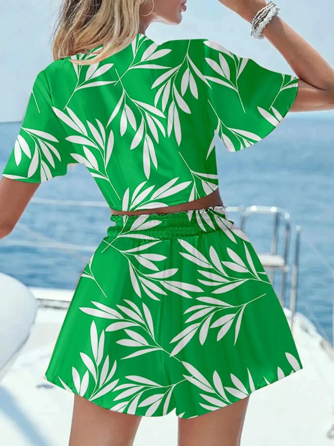 Woman wearing a green printed tie front top and shorts set with white leaf patterns on a boat.