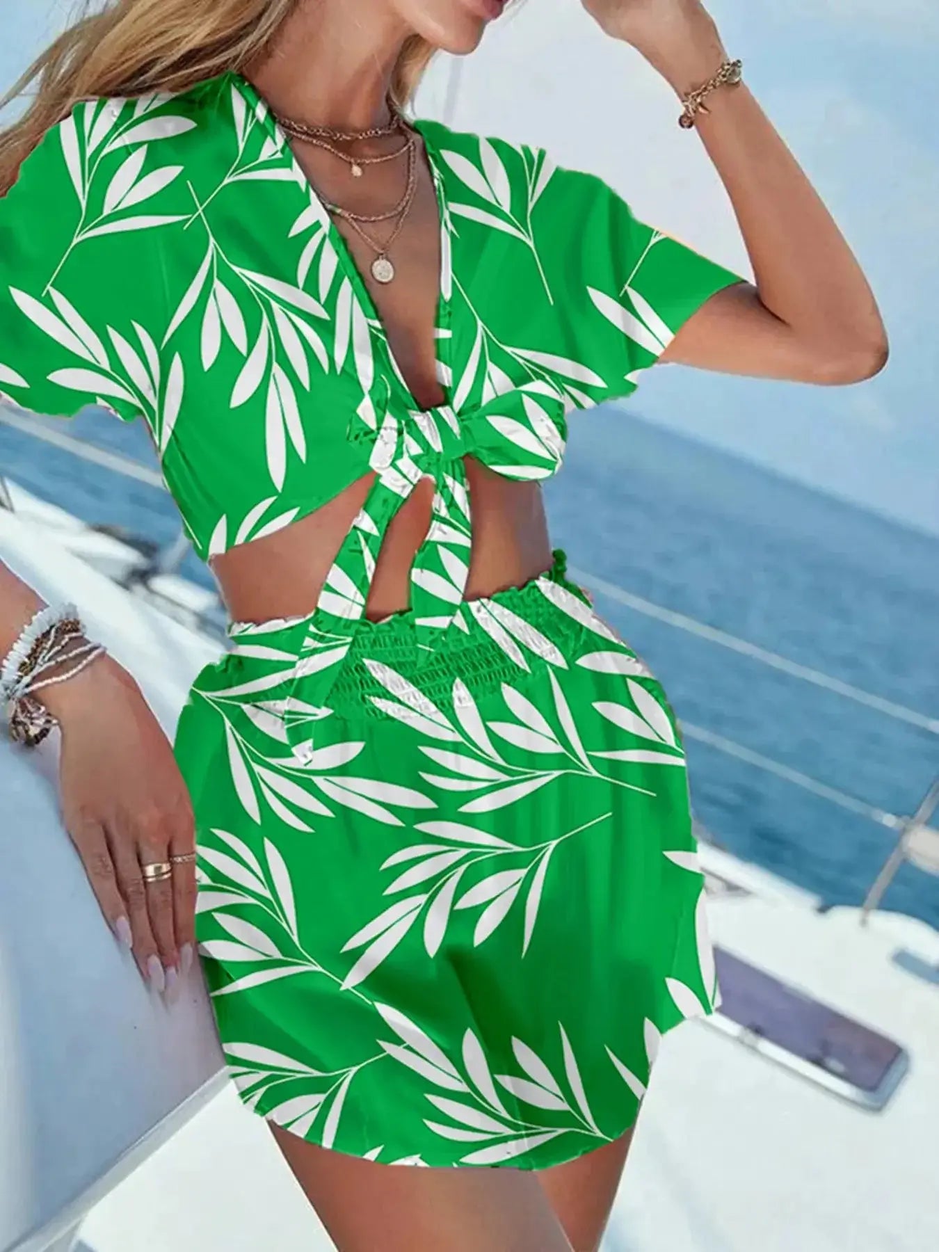 Woman wearing a green printed tie front top and shorts set against a maritime backdrop.