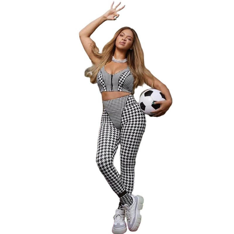 Woman in black and white checkered outfit holding a soccer ball, posing with a playful gesture.