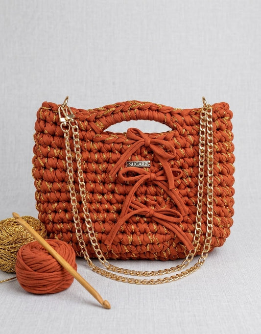 The Solstice Clutch, the orange bag with gold chain: “Orange woven Solstice clutch with front lacing and a gold chain strap.”