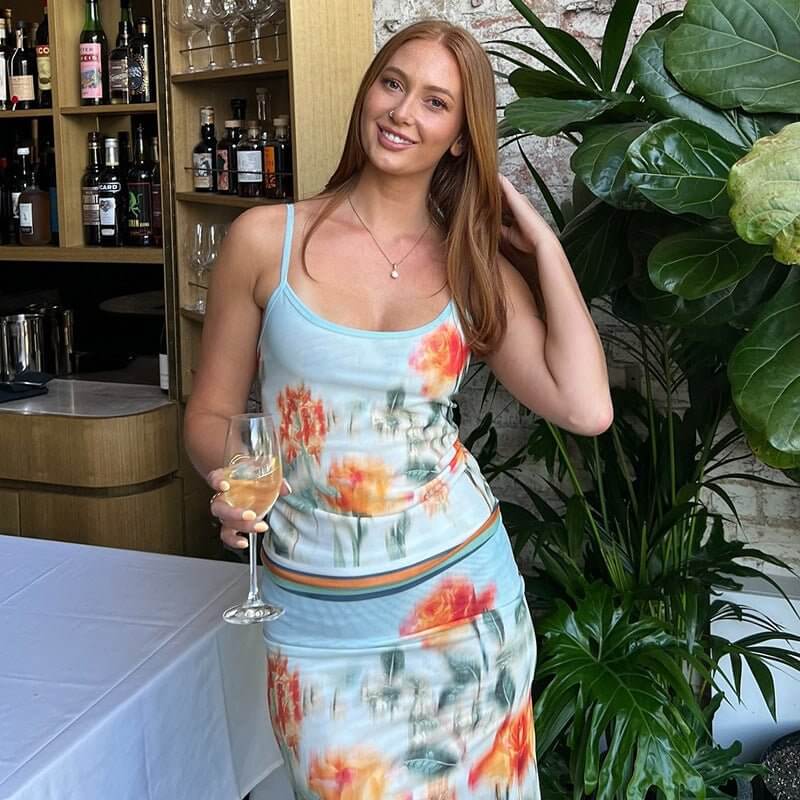Woman in cute printed contrast color slim fit sling sheath skirt outfit, holding a drink in a stylish setting.