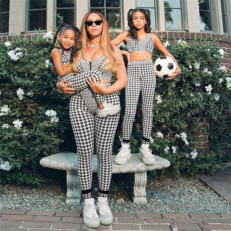 Stylish mother and daughters in matching black and white checkered outfits, one holding a soccer ball, posing outdoors.