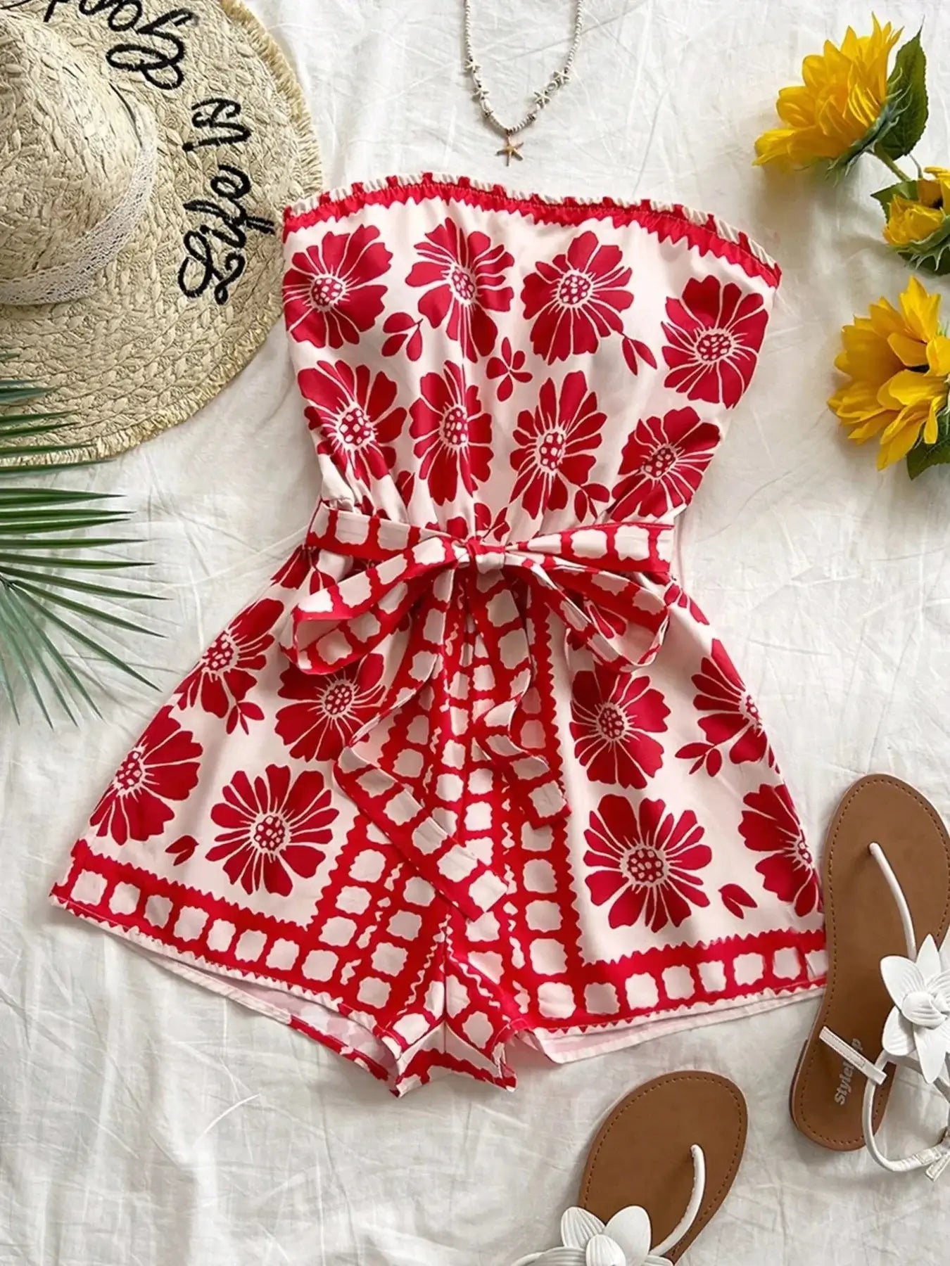 Printed tube tie waist romper with red floral pattern, perfect for summer beachwear. Styled with sun hat and sandals.